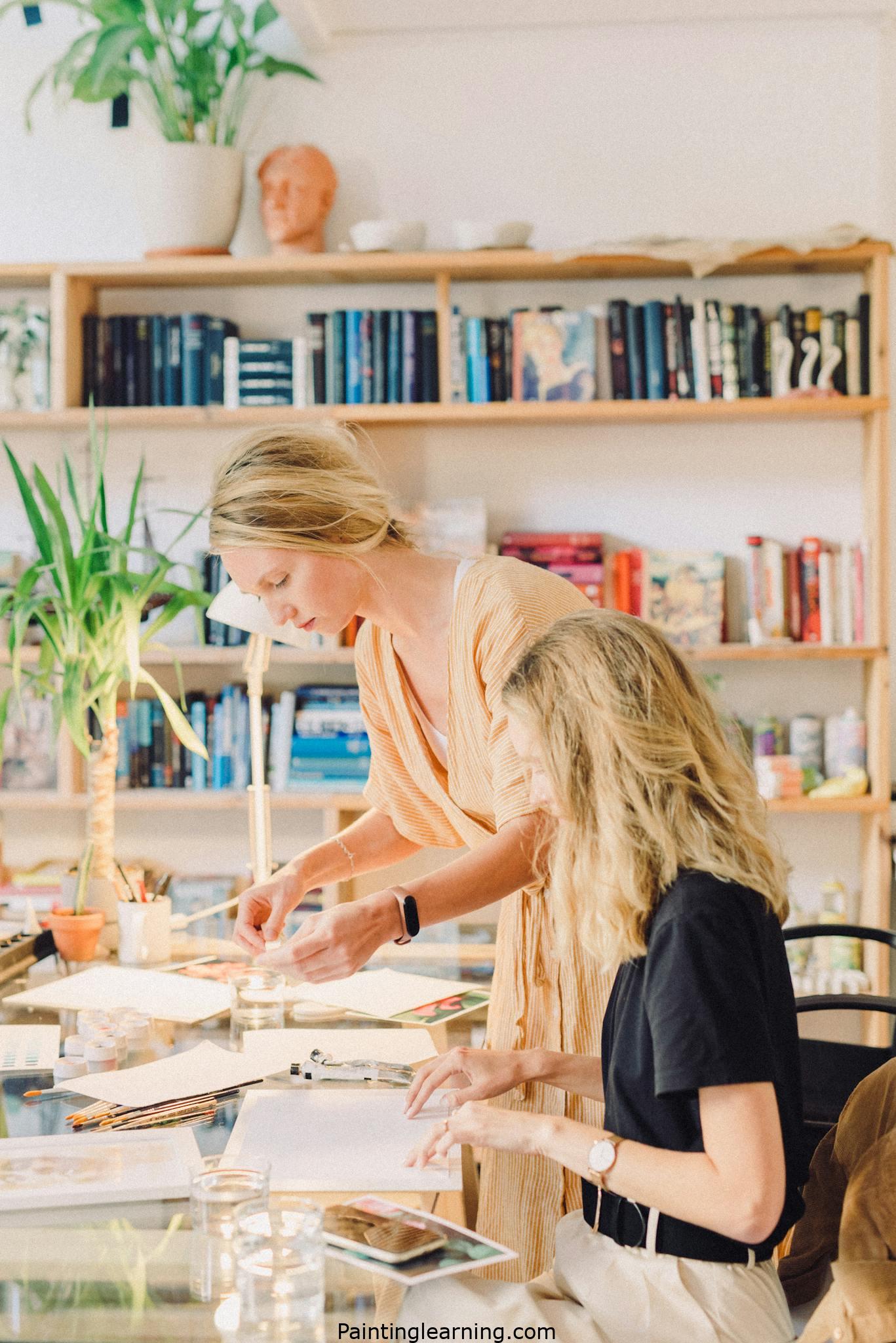Two women engaged in a watercolor painting activity in a bright, cozy library setting.